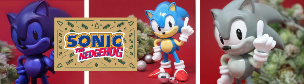 Trois figurines de Sonic reprenant la pose emblématique du personnage. Une en bleu sur le côté gauche, une figurine couleur classique au milieu et une dernière en coloris gris sur la droite. Une idée parfaite pour un cadeau de Noël. Le logo se trouve au premier plan.