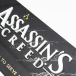 Lampe avec le logo du jeu vidéo Assassin's Creed, de la marque Neamedia Icons, vue de face, allumée dans un environnement sombre